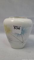 Front view of the white porcelain vase with hand-painted dandelion floral motifs in yellow, blue, and gray with a MaxSold lot number sticker visible on the front.