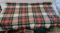 A full view of the light blanket laid out flat showing the entire tartan pattern and fringed edges.