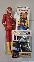 Four toys including The Flash figure, Ronan Funko Pop collectible in box, Ken doll partially visible behind The Flash, and Ernest the Bear toy in box