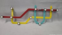 Front view of the multicolored coat rack showing yellow, red, and blue metal lines with attached hooks.