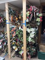 Photo showing several fall wreaths hung and stacked on a wooden rack with assorted ribbons and flower decorations