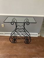 Full view of the black metal wine rack side table with glass top showing the rectangular glass surface and metal frame with integrated wine holders.