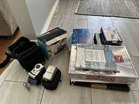 Photo showing Panasonic and Olympus digital cameras with their respective carrying cases along with stack of games and books including Monopoly and coloring books.