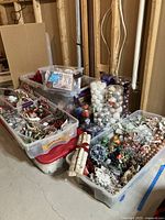 Multiple plastic bins filled with various Christmas wreath decorations, including artificial flowers, assorted ornaments, and other seasonal decor items.