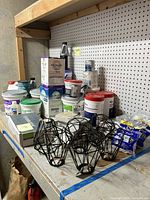 Photo showing a workbench with containers of grout, polyurethane, tile samples, blue bags of wallpaper activator, and black geometric metal light fixtures.