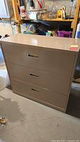 Front view of beige metal lateral file cabinet with three drawers and recessed handles.