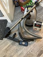 Full view of vacuum unit with wand, hose, main brush head, attachments and boxed bag on floor
