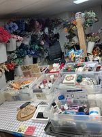 Overview of multiple bins with assorted wreath making supplies, artificial flowers arranged on wall in cones, and crafting tools on a table