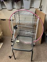 Two metal wire racks with multiple shelves, collapsible easel, pink hula hoop, and small outdoor table with glass top all shown in photo