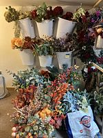 Wide shot showing artificial flowers in white plastic bins on a pegboard with additional flowers spread on the floor and a storage bag.