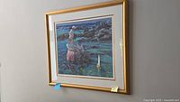 Framed numbered print showing the full artwork with beach scene, three people, and toy boat in gold tone frame on wall.