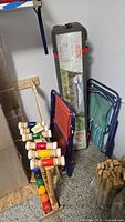 Photo showing Coleman tent in soft carrying bag with label, folded red and green outdoor chairs, Sportcraft croquet mallets and balls on rack, and bubble bottle.