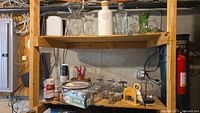 Wide view of wooden shelving unit holding various clear glass vases, Ball jars, ceramic pots, candle holders, and paper goods.