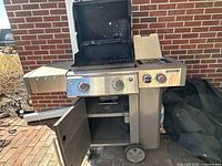 Front angle of stainless steel grill with lid open, side shelf, open cabinet and wheels visible