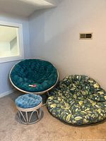 Photo showing teal cushioned Papasan chair, floral cushion, and matching wicker ottoman, all on carpeted floor against light purple wall.
