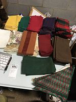 Top view of assorted cloth napkins arranged in sets by color and pattern on a white table, including solid yellow, green, red, purple, brown, plaid red and green, and floral patterns.