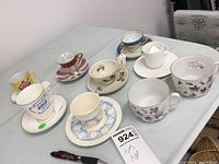 Photo showing the assortment of 8 teacups with 3 additional saucers on a table, close-up view of patterns and shapes.