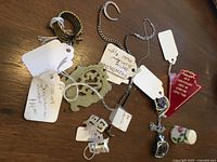 Photo showing assorted small collectibles and jewelry including pendants with tags, twisted rope style jewelry piece, red scouting exposition badge, and porcelain floral thimble on wooden surface.