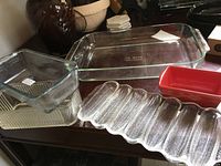 Overview of several glass bakeware pieces including the large Pyrex rectangular dish, smaller glass dishes, a red cornbread dish, and a textured glass tray.