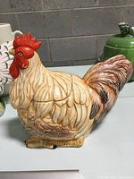 Full view of the rooster cookie jar showing light brown and cream feather detailing with bright red comb and wattles, standing on yellow feet.