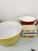 Yellow large ceramic mixing bowl, red measuring jug, and three small decorative ceramic baking dishes