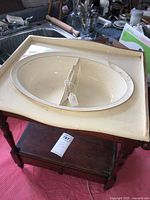 Front view of wooden child's wash stand with cream ceramic divided basin on top, showing visible crack in basin, wooden drawer below, and towel racks.