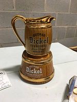 Full view of George Dickel ceramic whisky pitcher on matching base showing front branding and overall condition on grey background.