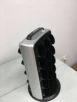 Front and side view of the black and silver plastic Keurig K-Cup holder carousel showing circular compartments for holding K-Cups in a grid layout and rotating base.