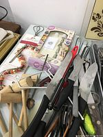 Collection of kitchen knives, skewers, wooden mallets, scissors, and utensils closely grouped on a white surface