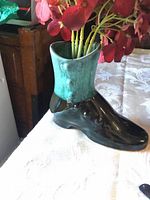 Mini ceramic vase shaped like a boot with green glaze on upper part and brown lower part, filled with artificial red flowers.