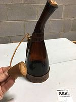 Amber glass whiskey decanter with curved neck and embedded Tennessee Dickel leather branding on bands around the neck and base, cork stopper with leather covering attached to leather strap held by hand.