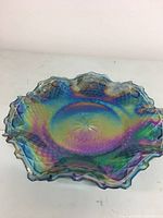 Top and angled view of multicolor iridescent carnival glass bowl with diamond cut pattern and starburst center. Edged with ruffled shape.