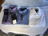 Three folded Kenneth Cole dress shirts (purple, blue, white) and four pairs of unopened dress socks laid flat on white surface.