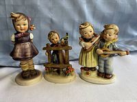 Three vintage Goebel Hummel figurines arranged side by side against a blue cloth background, showing full frontal view of each figurine.