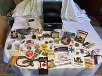 Wide view of lot items spread on table with black storage box, carved duck decoy, A&W bear figurine, various pins, patches, stickers, and other collectibles