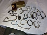 All jewelry items including watch, ring, fossil necklace and multiple bracelets arranged on white cloth
