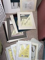 Pile of various mats on floor, some still in packaging, mostly white, cream, black, and grey colors