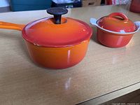 Side view of the orange cast iron saucepan with lid alongside the mini croc pot.
