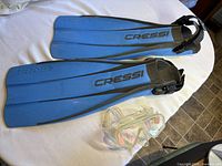 Pair of blue Cressi Frog snorkeling flippers and clear snorkel mask displayed on white surface