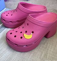 Pair of pink Crocs platform heels featuring a yellow banana charm on the front ventilation holes, showing overall condition and design.