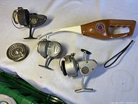 Five fishing reels and combo laid on white surface; includes brown and white Pocket Fisherman rod and reel, black and silver spinning reels with vintage look