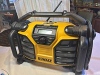 Front view of DeWalt multi-purpose charger showing display, control buttons, radio antenna, and speaker grills with protective black handles.