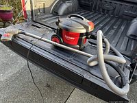 Photo showing the full vacuum unit including the hose and metal wand, placed on the bed of a black Ford truck for scale and clarity.