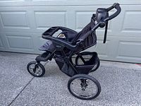 Side view of the black Graco 3-wheel jogging stroller, showing large air-filled tires, front swivel wheel, storage basket, and parent tray with cup holders.