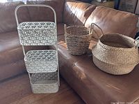 Wide shot showing metal storage organizer with semi-circle fan pattern next to two woven seagrass baskets on a leather couch.