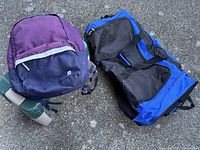 Large rolling duffle bag and small backpack shown on pavement surface, highlighting size and colors.