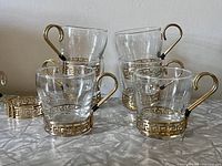Front view of all six Libbey Greek key coffee cups arranged showing glass and gold metal wrap and handles.
