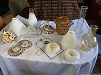 Full lot view showing assorted vintage light fixture parts including glass shades, chimneys, bases, and a decorative ceramic finial.