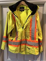 Front view of the yellow hi-vis coat with orange and silver reflective stripes and black inner collar, hung on hanger.