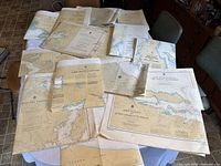 Photo showing 15 large folded navigation charts spread on a table with visible map details including various local British Columbia coastal areas.